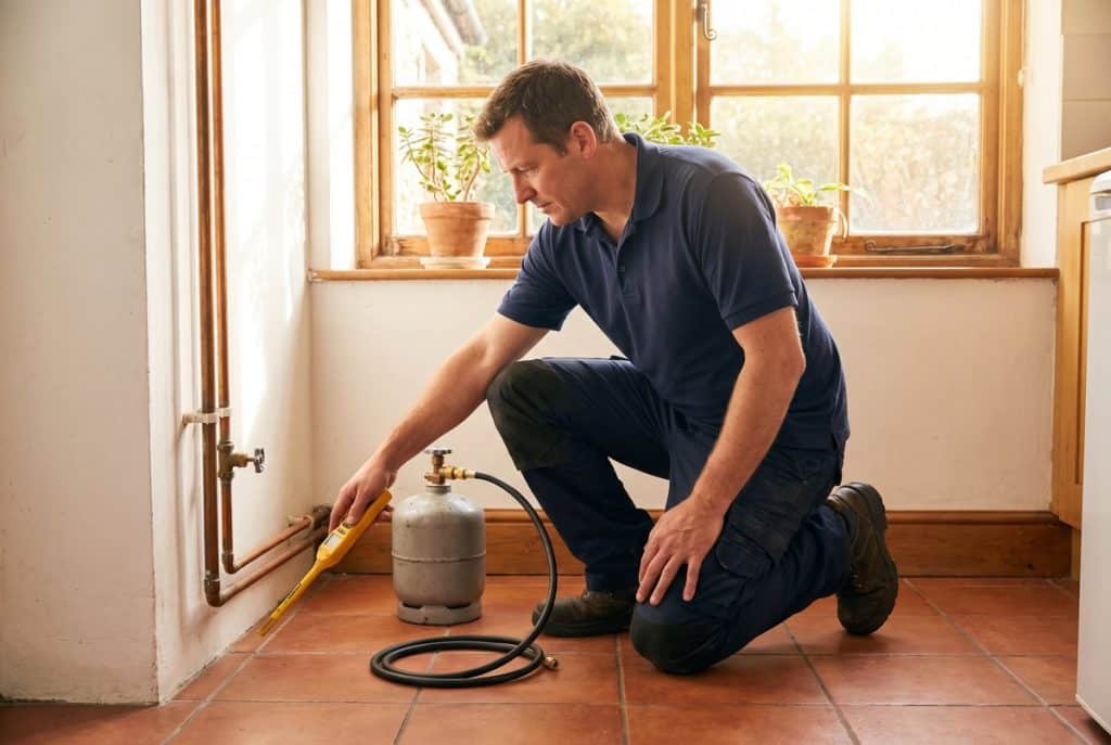 Leak detection engineer holding a hydrogen tracer gas detector probe beside a heating pipe