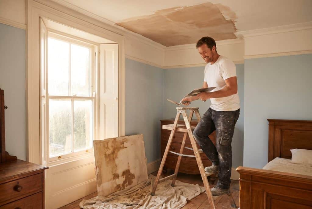 Plasterer skimming a repaired section of ceiling after a water leak